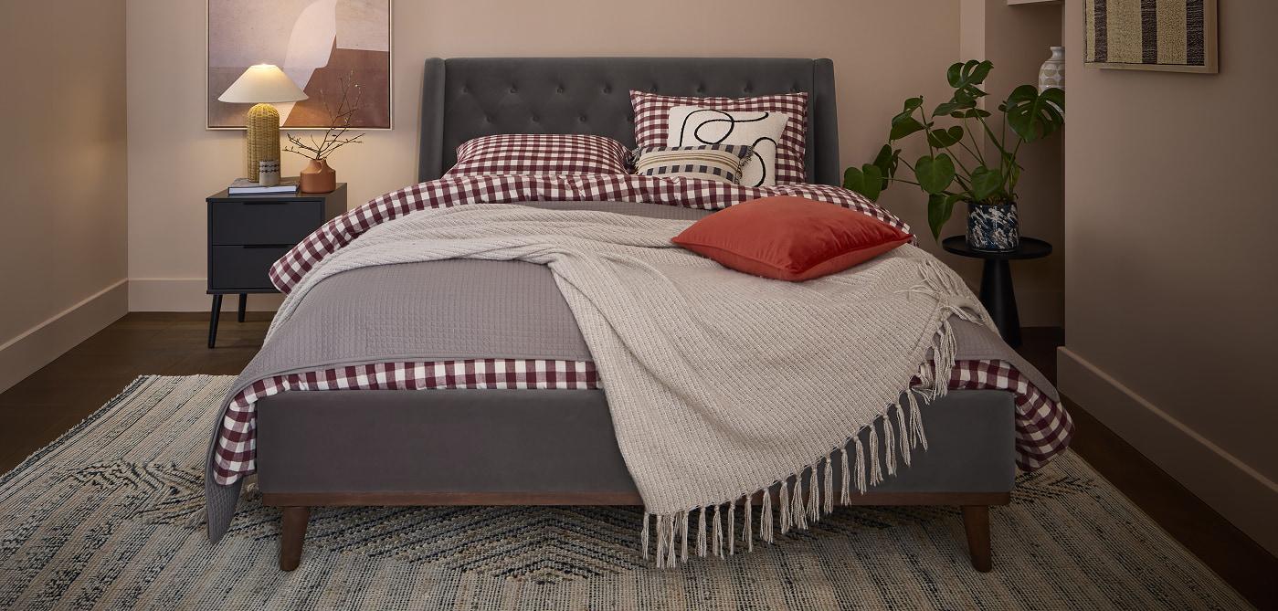 Chiswick bed upholstered in grey velvet, dressed with red gingham bedding and a cream throw