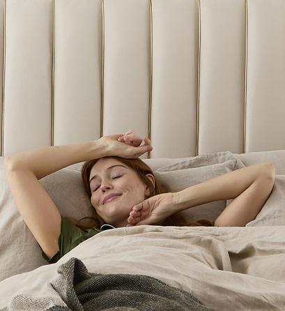 Woman waking up and stretching in an Altea bed with a fluted cream headboard