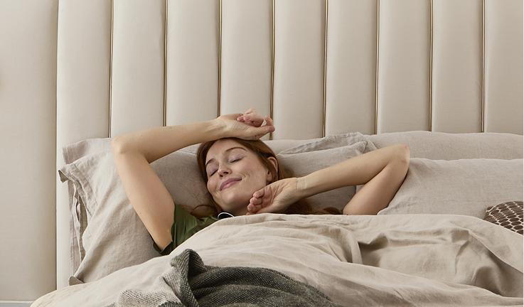Woman waking up and stretching in an Altea bed with a fluted cream headboard